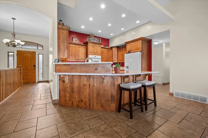 Kitchen featuring a breakfast bar, hanging lights, light countertops, wood finish cabinets, and white appliances
