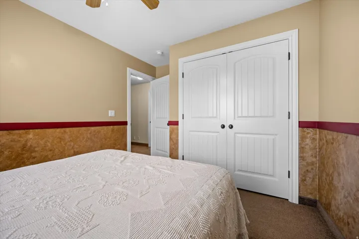 Carpeted bedroom with a wainscoted wall, a closet, and ceiling fan