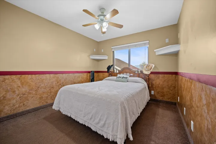 Carpeted bedroom featuring ceiling fan and wainscoting