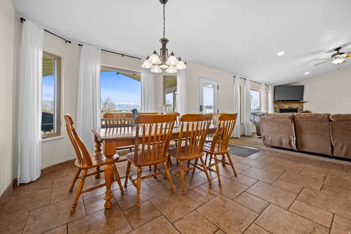 Dining room featuring vaulted ceiling, stone tile flooring, suspended lighting, a ceiling fan, and a fireplace