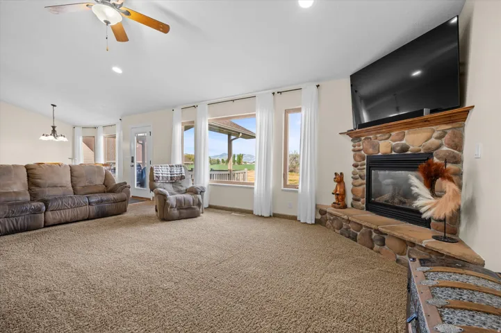 Carpeted living room with a ceiling fan, a stone fireplace, lofted ceiling, and suspended lighting