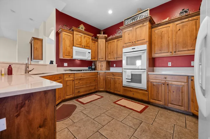 Kitchen featuring white appliances, a peninsula, wood finish cabinetry, and light stone counters