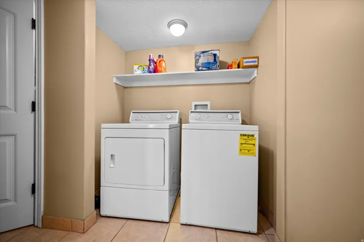 Laundry area with a textured ceiling, washing machine and clothes dryer, and light tile patterned floors