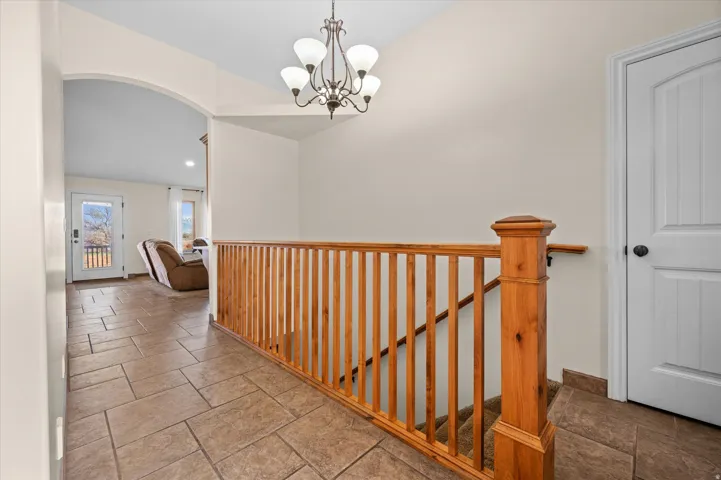 Hall featuring suspended lighting, stone tile flooring, arched walkways, an upstairs landing, and lofted ceiling