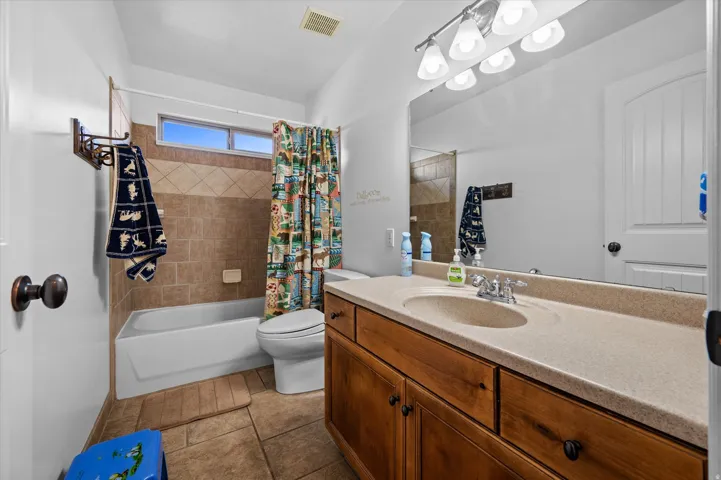 Full bath with vanity, shower / bath combination with curtain, and dark tile patterned flooring