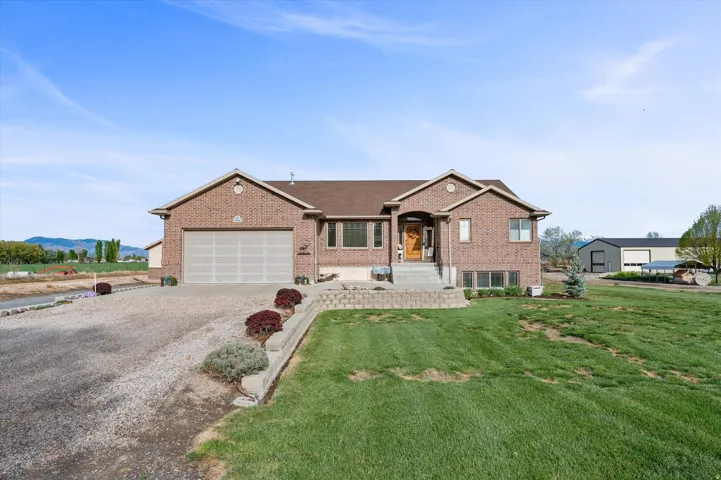 Ranch-style home with gravel driveway, brick siding, a front yard, and an attached garage