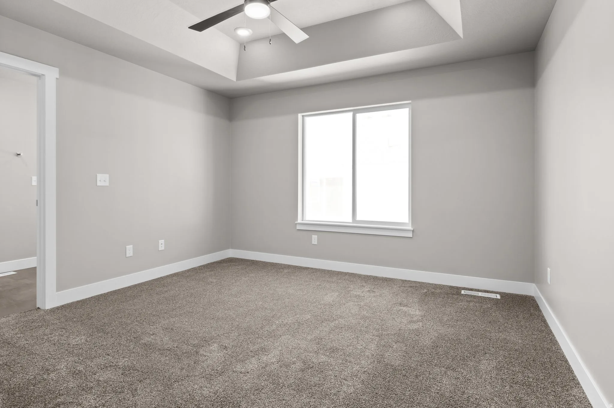 Neutral-toned room featuring a tray ceiling with recessed lighting and a ceiling fan