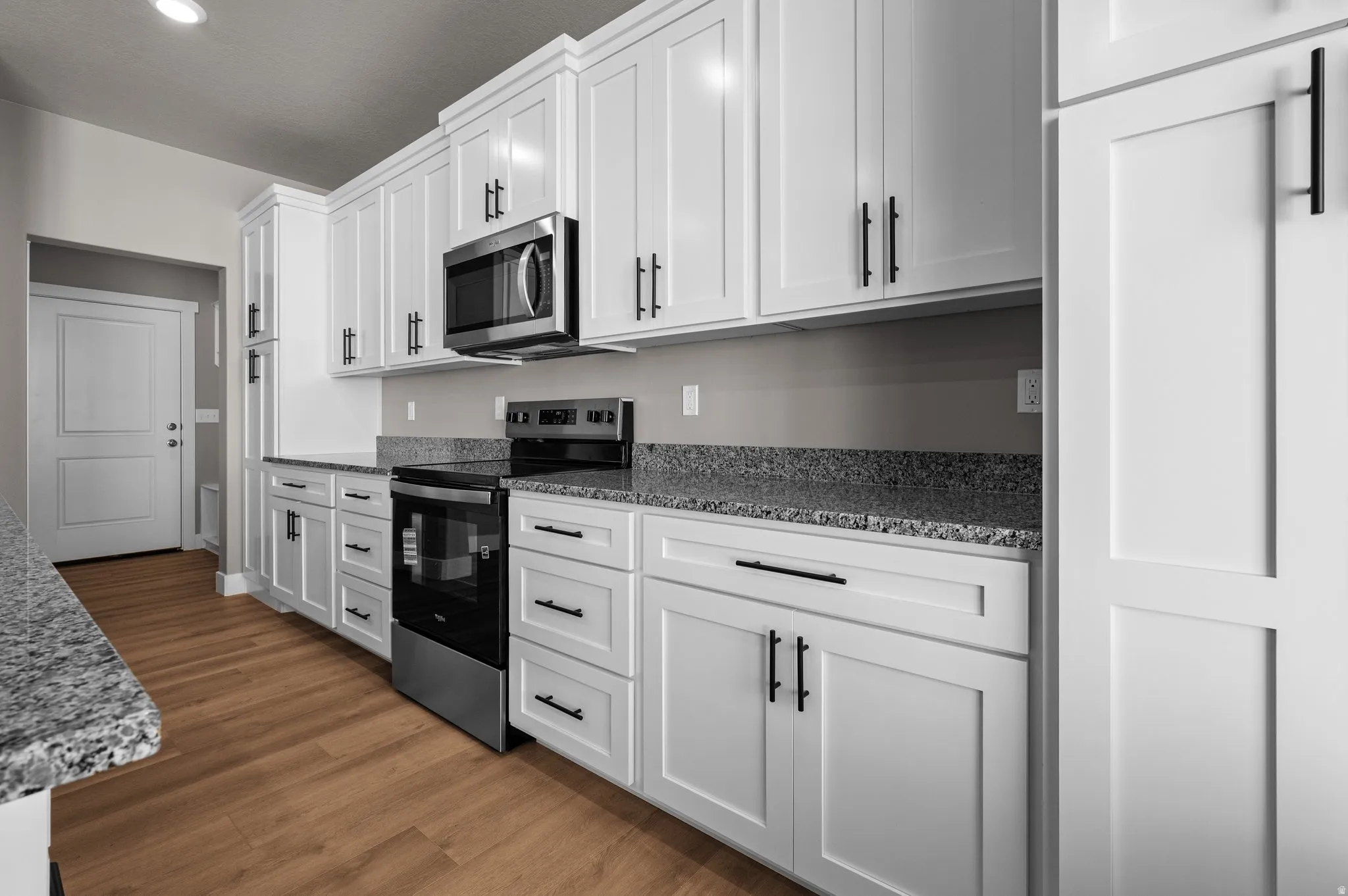 Kitchen featuring white shaker cabinetry, stainless steel appliances, speckled stone countertops, and wood-finish flooring