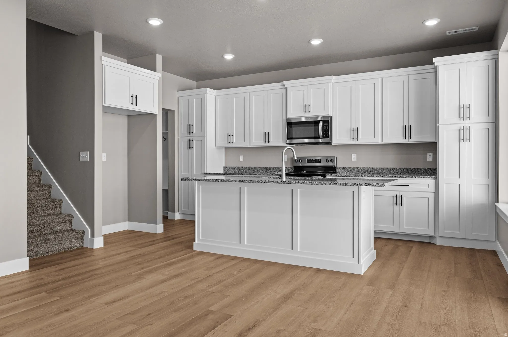 Kitchen featuring white cabinetry, a central island, stainless steel microwave, and wood-finish flooring