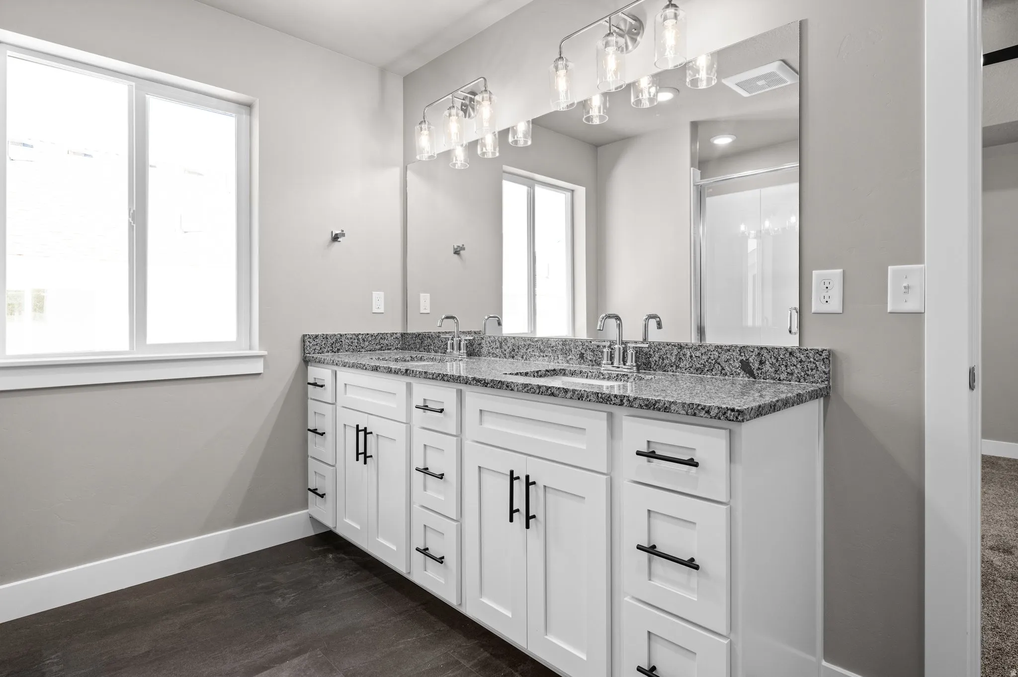 Spacious bathroom featuring a double vanity with granite countertop, dual undermount sinks, and contemporary wall-mounted lighting