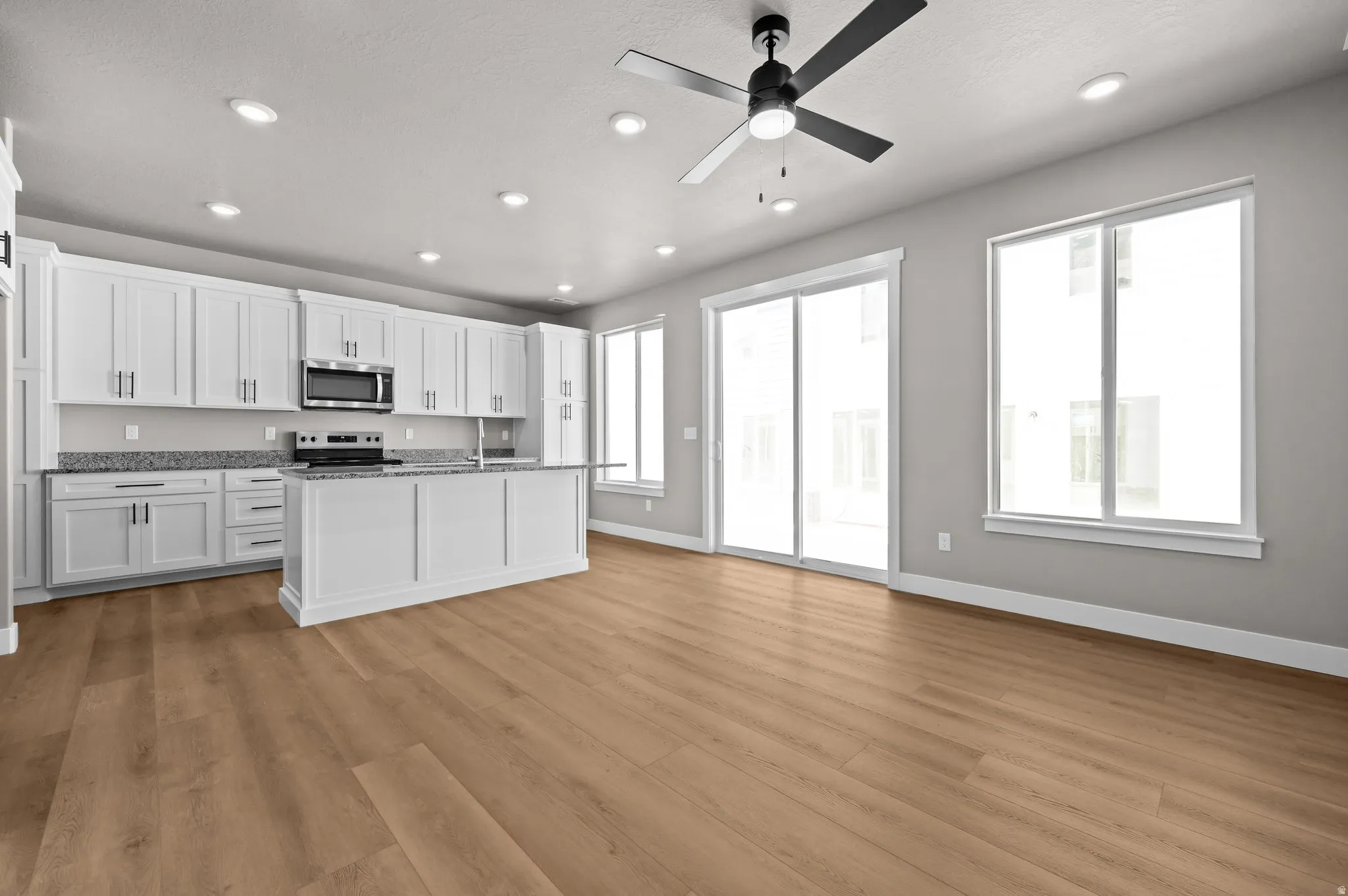 Open-concept living space featuring a modern kitchen with white cabinetry, stainless steel appliances, and stone countertops