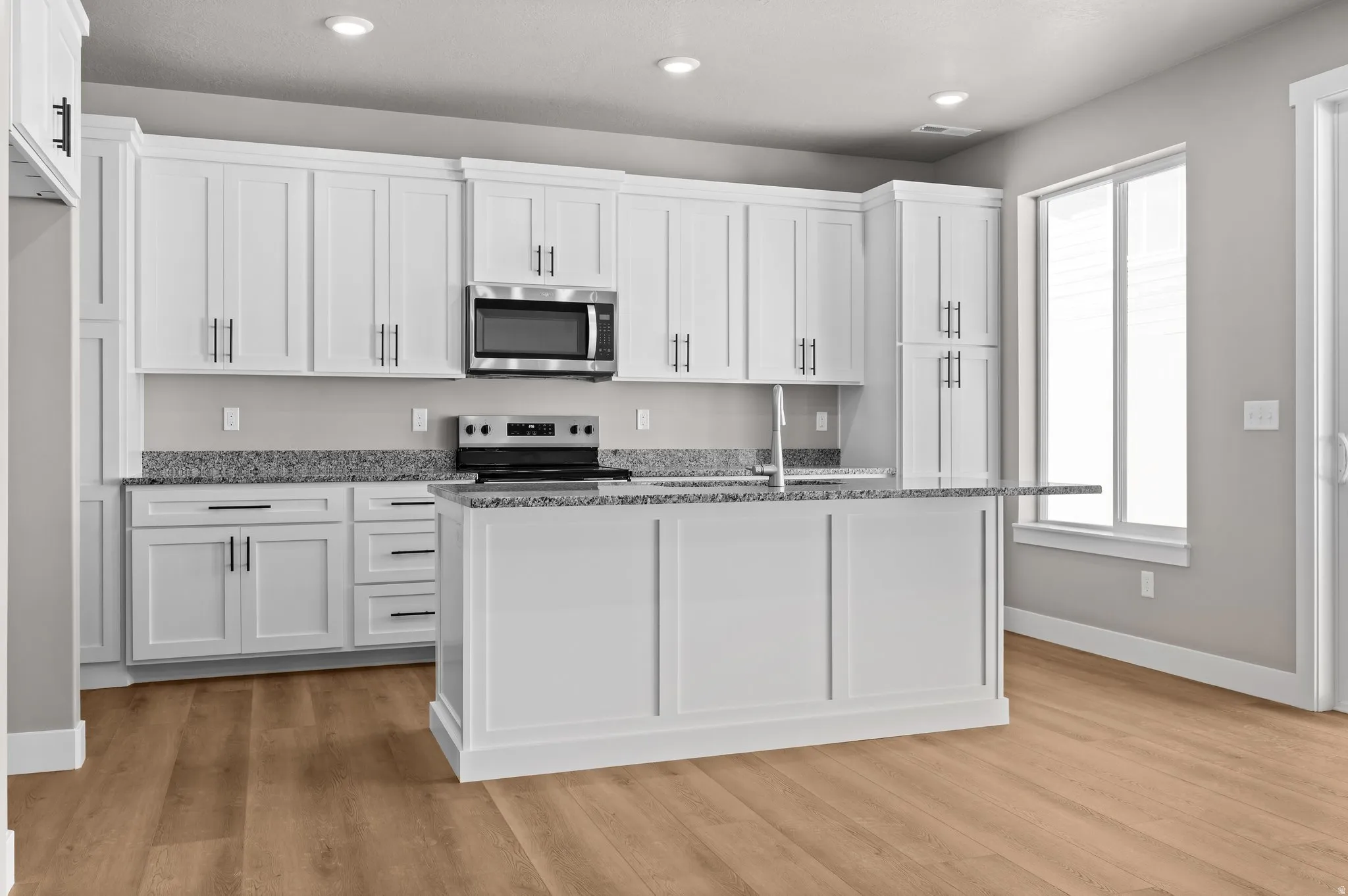 Kitchen with white shaker cabinetry, stainless steel microwave, black electric range, and light-toned wood-finish flooring