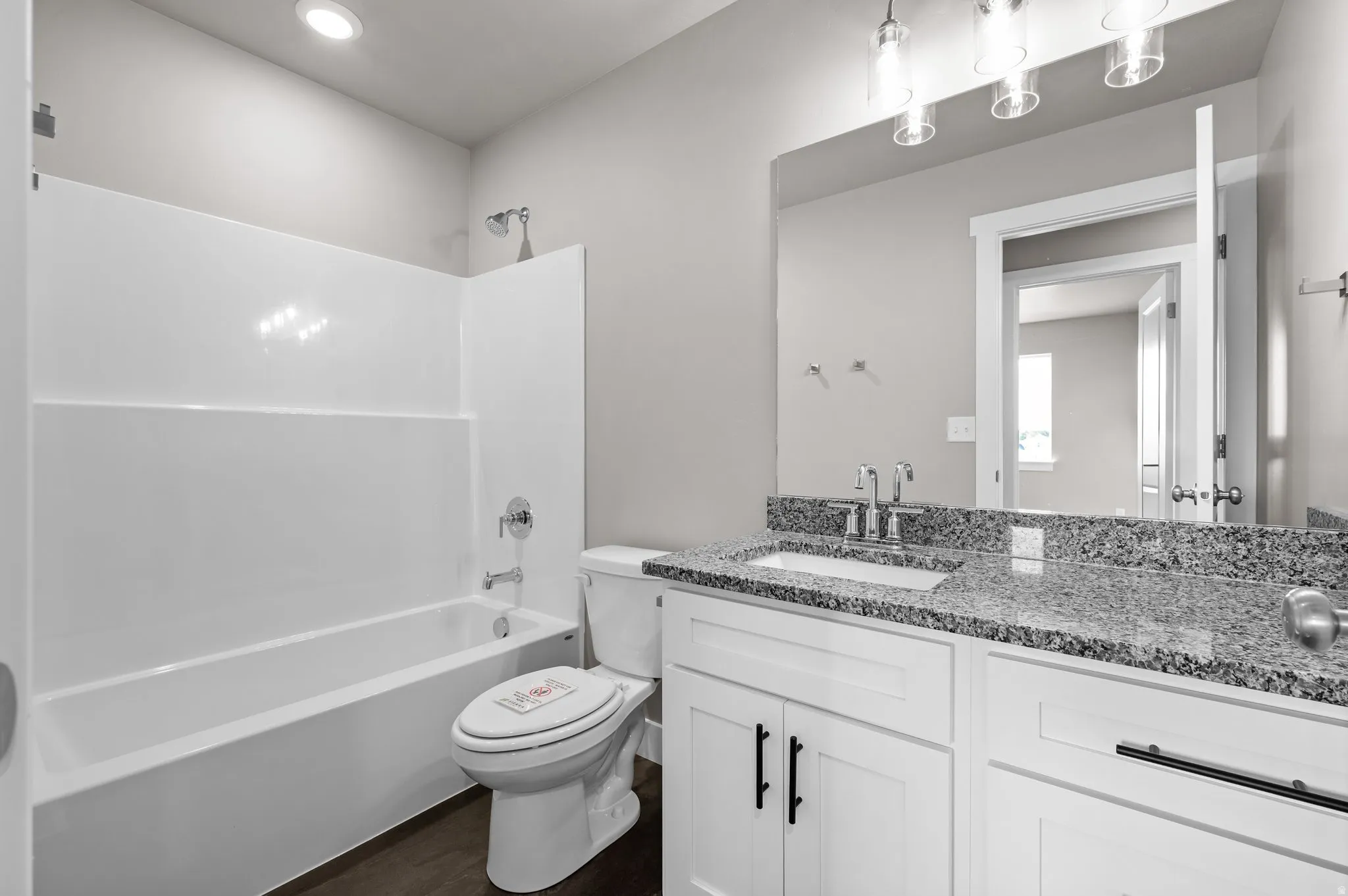Bathroom featuring a white bathtub/shower combination, a vanity with a granular stone countertop, a rectangular undermount sink with a chrome faucet, a large wall-mounted mirror, and white cabinetry with dark hardware