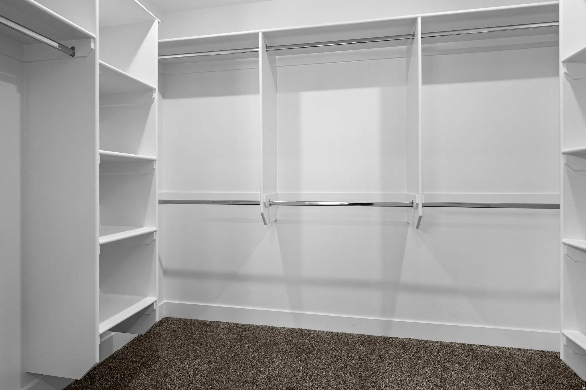 Custom-built closet system featuring white shelving units, multiple chrome hanging rods, and dark carpeting