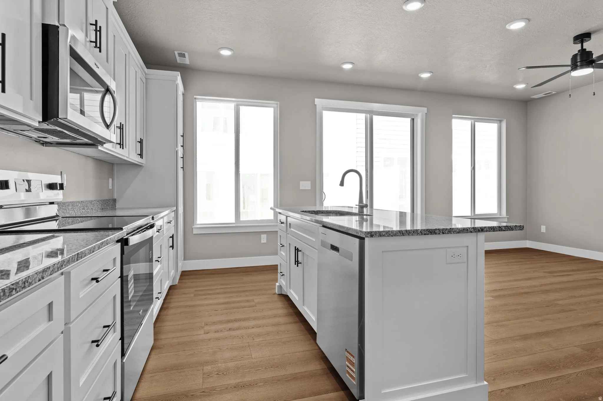 Modern kitchen featuring white cabinetry, stainless steel appliances, granite countertops, and wood-finish flooring