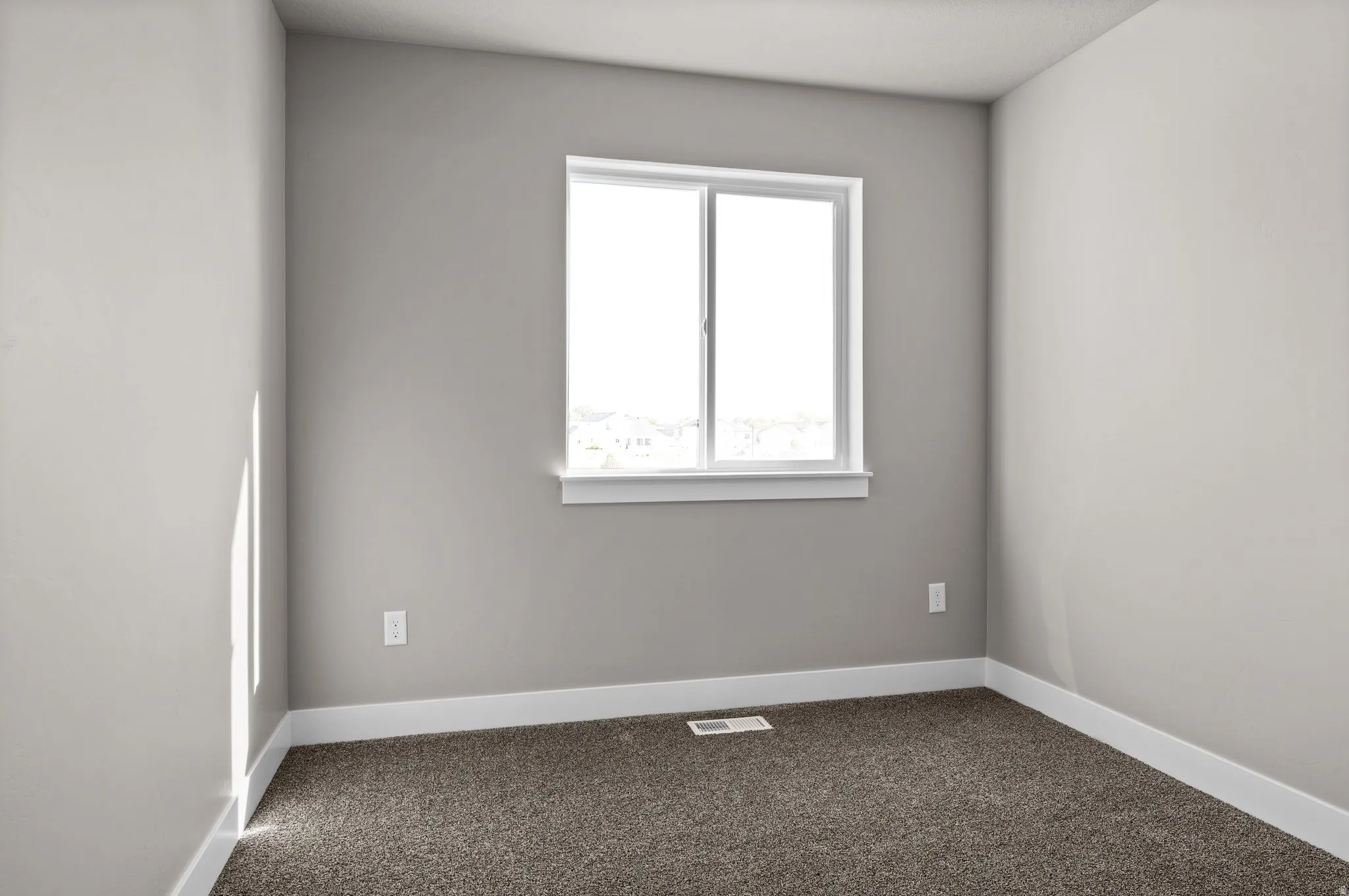 Neutral gray walls with white trim and a single window, complemented by brown carpet flooring