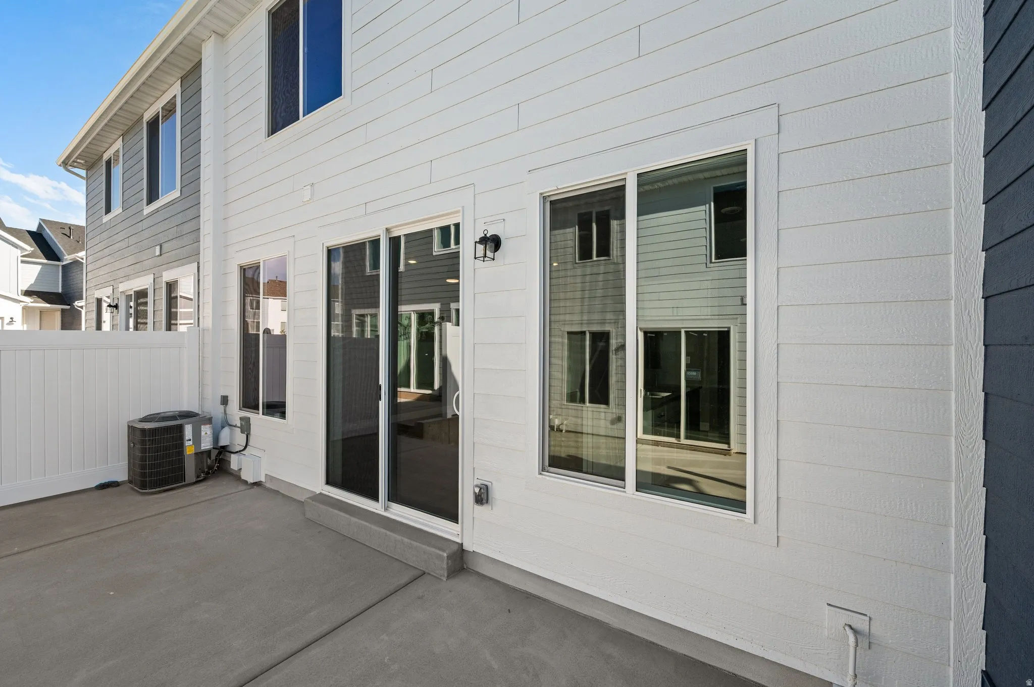 Concrete patio with a white vinyl privacy fence, white siding, and a sliding glass door