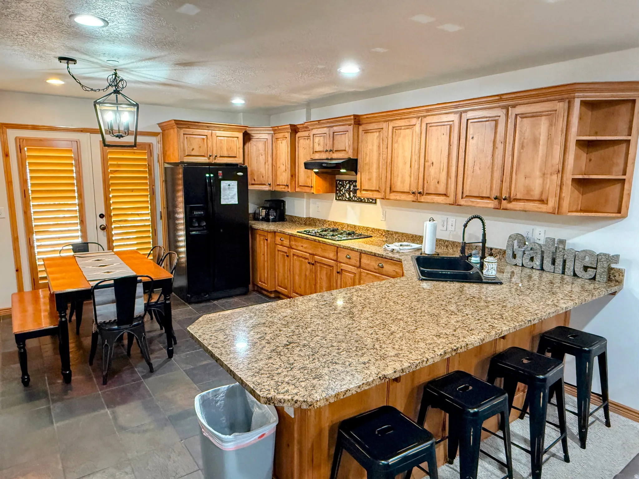 Kitchen with open shelves, a kitchen bar, black refrigerator with ice dispenser, wood finish cabinets, and a peninsula