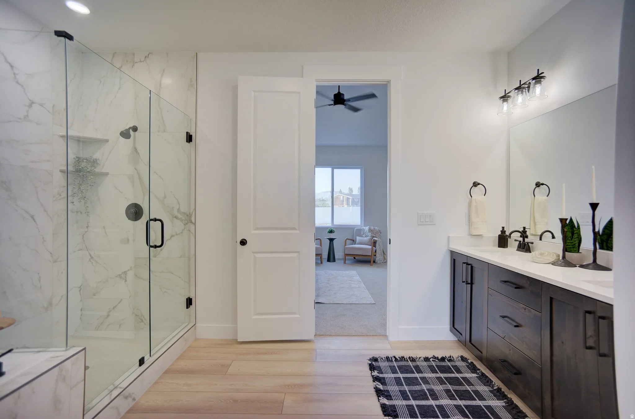 Ensuite bathroom featuring double vanity, a marble finish shower, light wood-type flooring, ceiling fan, and recessed lighting