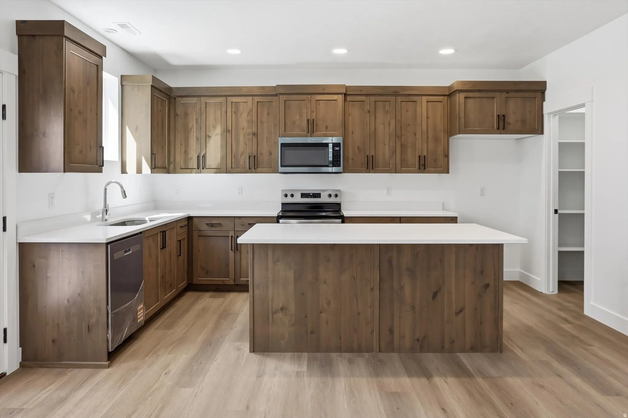 Kitchen with stainless steel appliances, light wood-style floors, a center island, recessed lighting, and wood finish cabinets