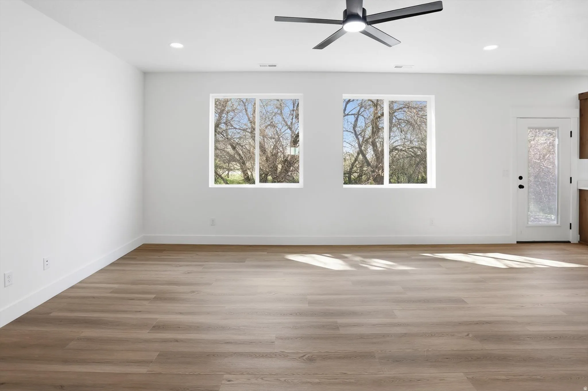 Empty room with a ceiling fan, light wood-style flooring, healthy amount of natural light, and recessed lighting