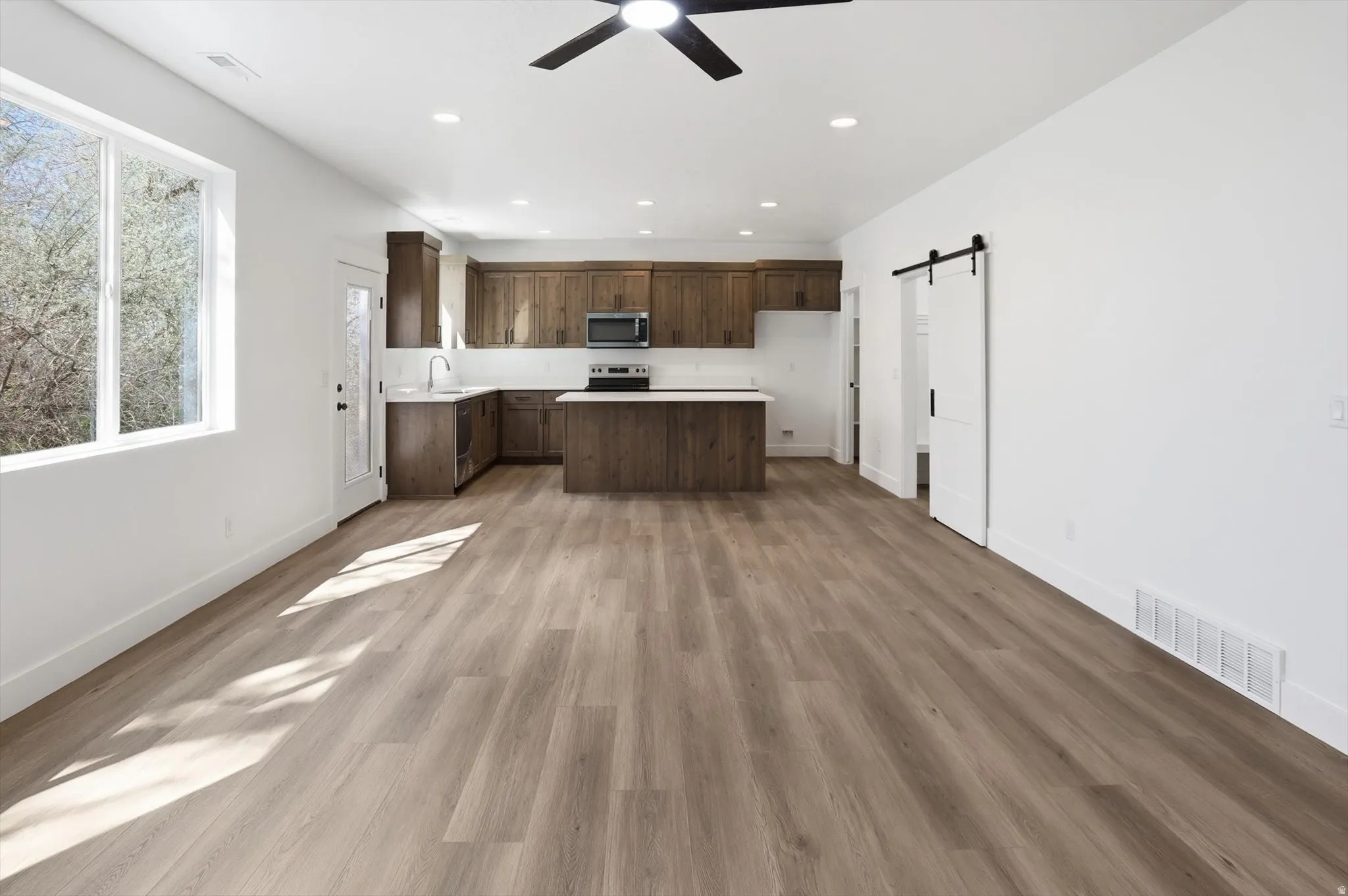 Kitchen featuring a barn door, light countertops, a ceiling fan, dark wood finish cabinets, and a kitchen island