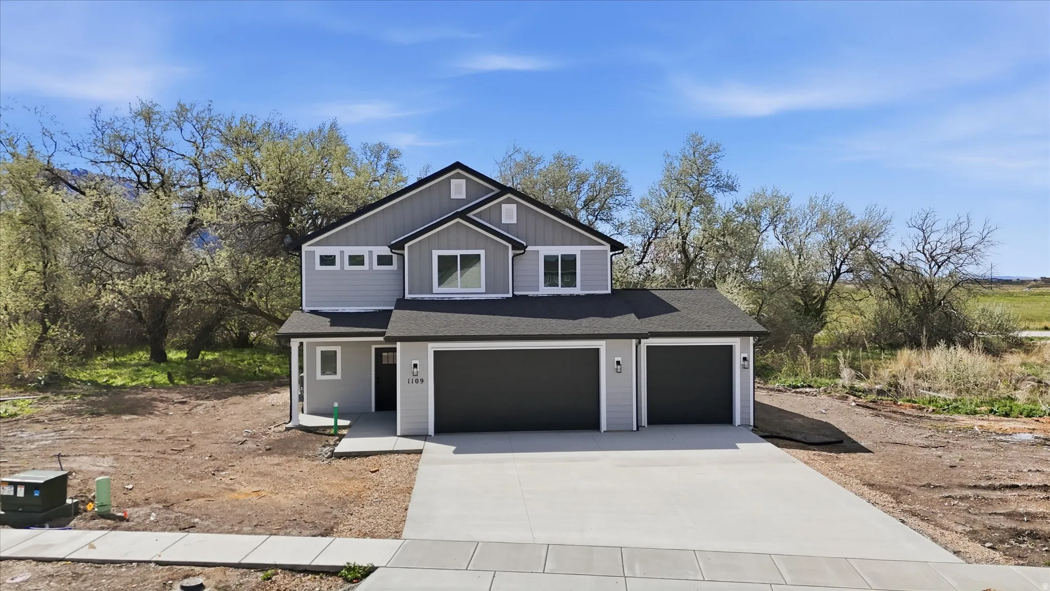 View of front of property featuring driveway, an attached garage, roof with shingles, a garage, and board and batten siding