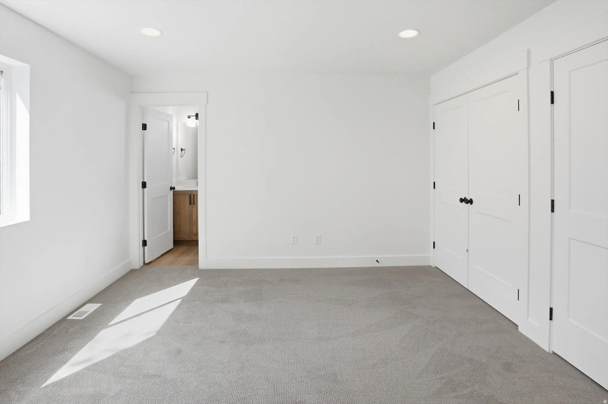 Unfurnished bedroom with light carpet, recessed lighting, ensuite bath, and multiple closets
