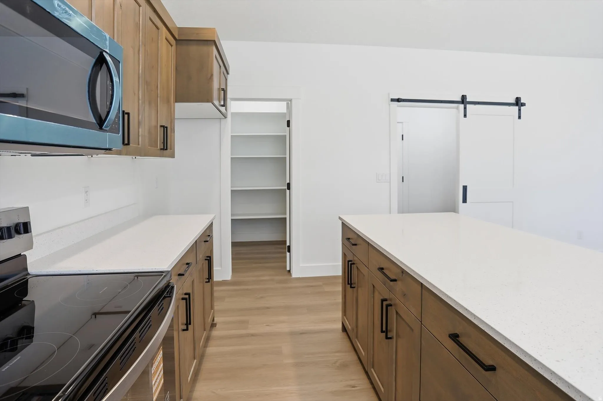 Kitchen with stainless steel appliances, a barn door, wood finish cabinets, light wood-style flooring, and light stone counters