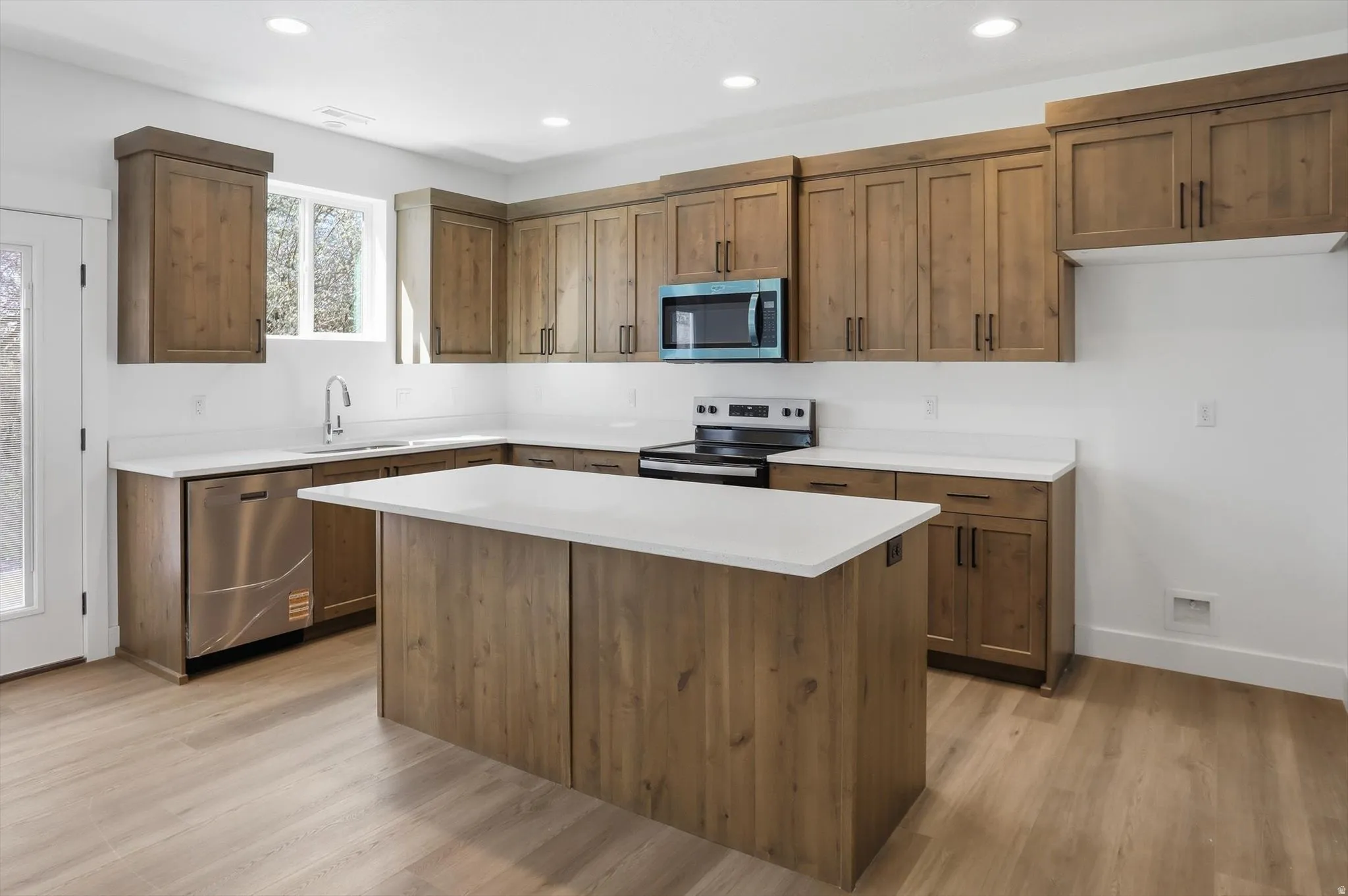 Kitchen featuring stainless steel appliances, a center island, light wood-type flooring, wood finish cabinets, and recessed lighting
