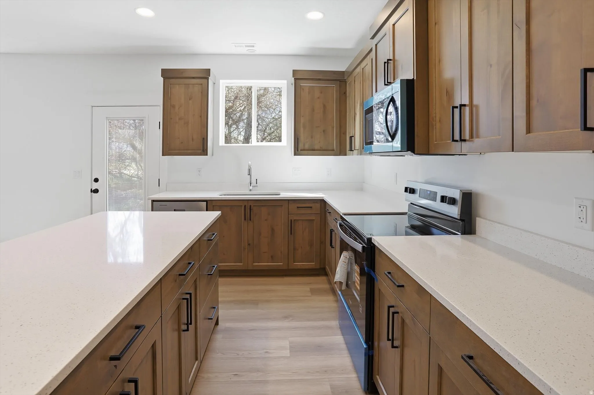 Kitchen with black electric range oven, wood finish cabinets, stainless steel microwave, and recessed lighting