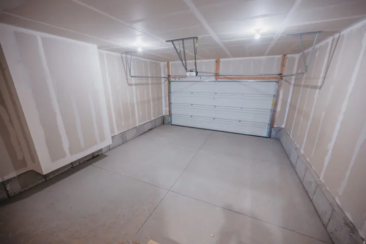 Spacious garage with an automatic overhead door, raw concrete flooring, concrete block foundation, exposed drywall, and ceiling-mounted lighting