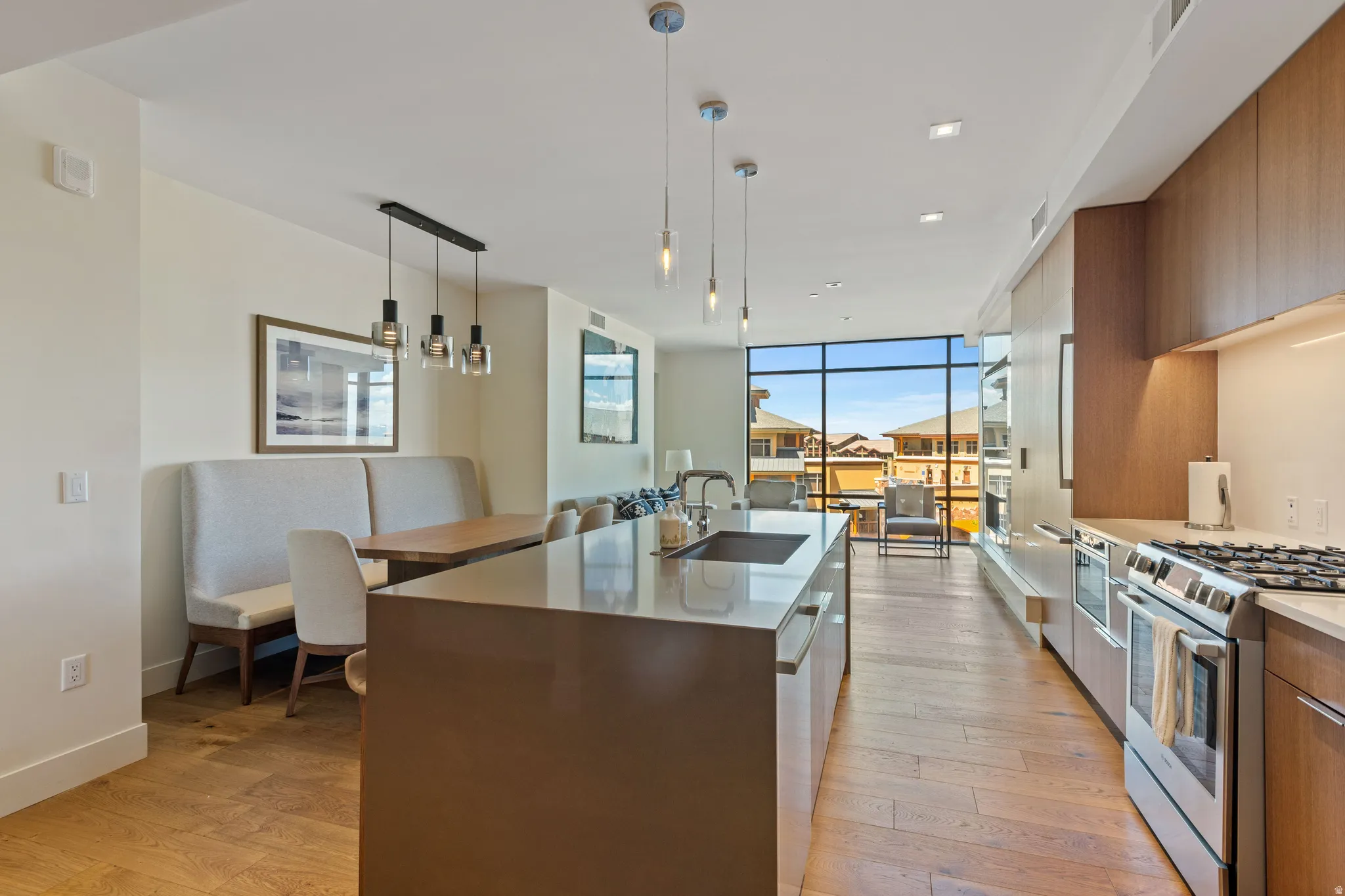Kitchen with modern cabinets, stainless steel appliances, expansive windows, light stone countertops, and a kitchen island with sink