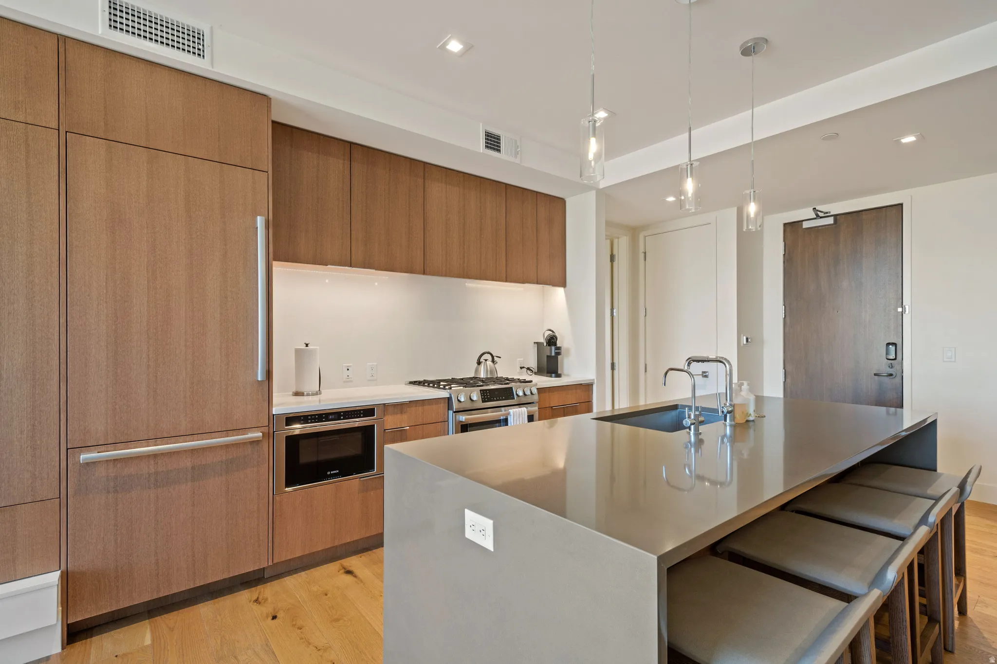 Kitchen with wood finish cabinets, a breakfast bar, light wood-style flooring, an island with sink, and pendant lighting