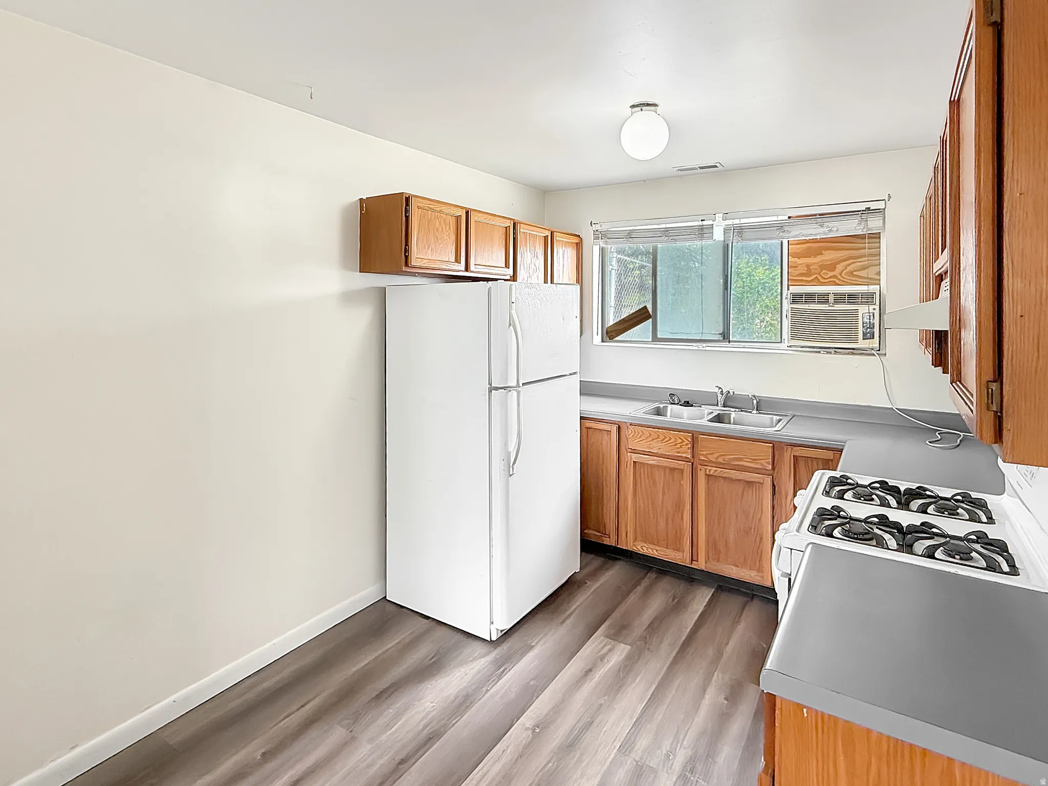 Kitchen with freestanding refrigerator, wood finish cabinetry, light wood-style floors, and light countertops