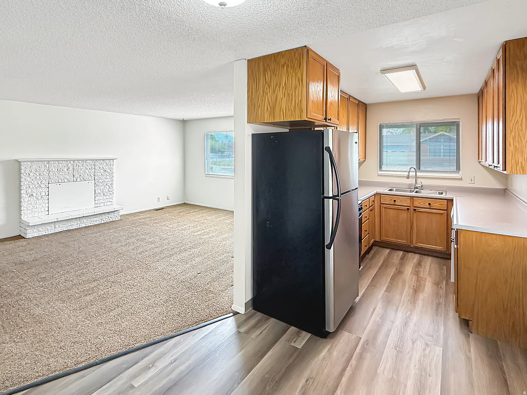 Kitchen with wood finish cabinetry, freestanding refrigerator, light countertops, a textured ceiling, and light wood-style flooring