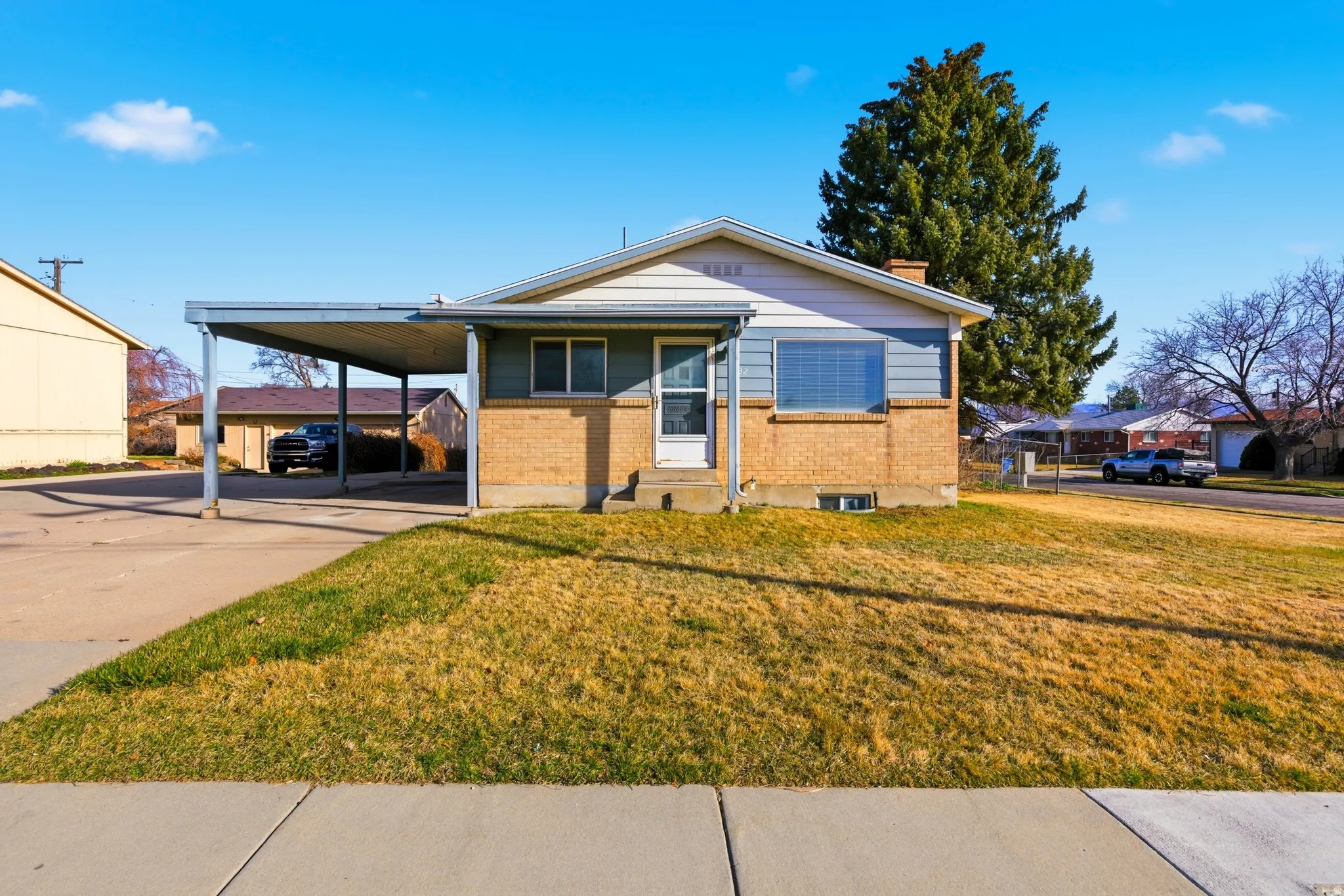 View of front of house with brick siding, a carport, a front yard, and concrete driveway