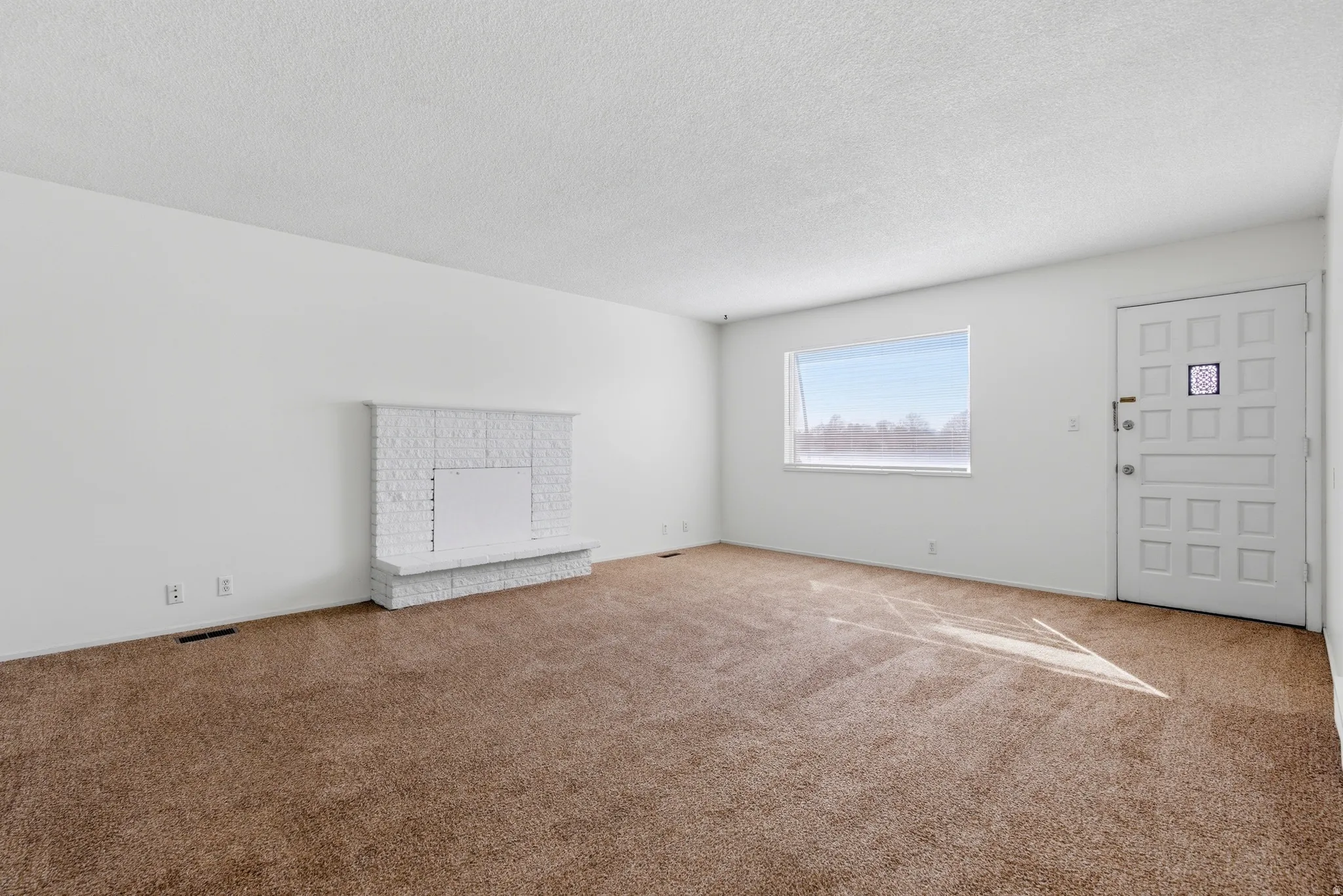 Unfurnished living room with carpet floors, a textured ceiling, and a brick fireplace