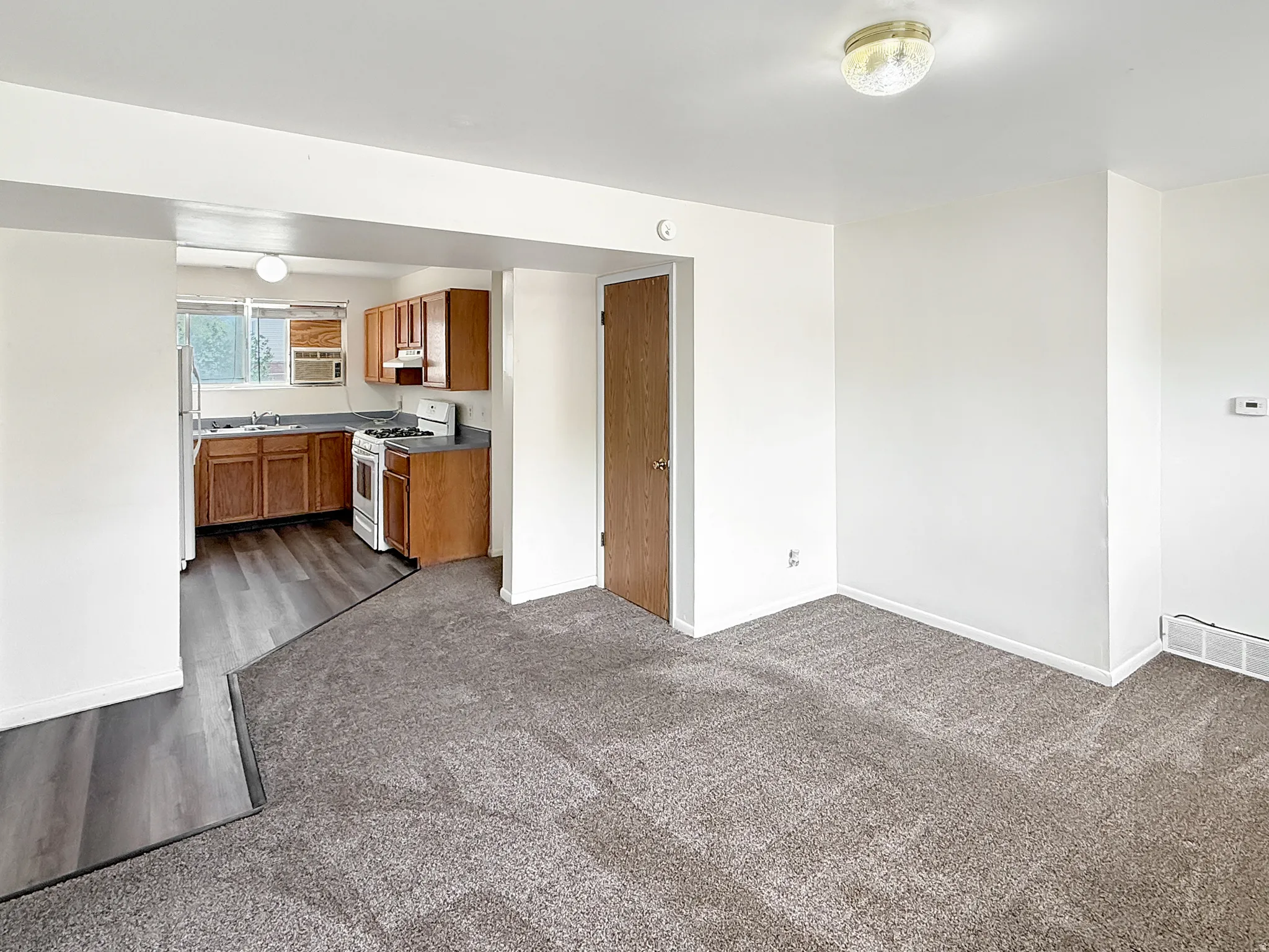 Kitchen featuring wood finish cabinetry, white appliances, dark carpet, and open floor plan