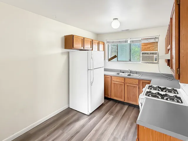 Kitchen with freestanding refrigerator, wood finish cabinetry, light wood-style floors, and light countertops