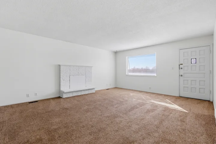 Unfurnished living room with carpet floors, a textured ceiling, and a brick fireplace