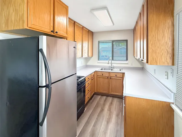 Kitchen featuring freestanding refrigerator, light countertops, wood finish cabinetry, black range with gas stovetop, and light wood-style floors