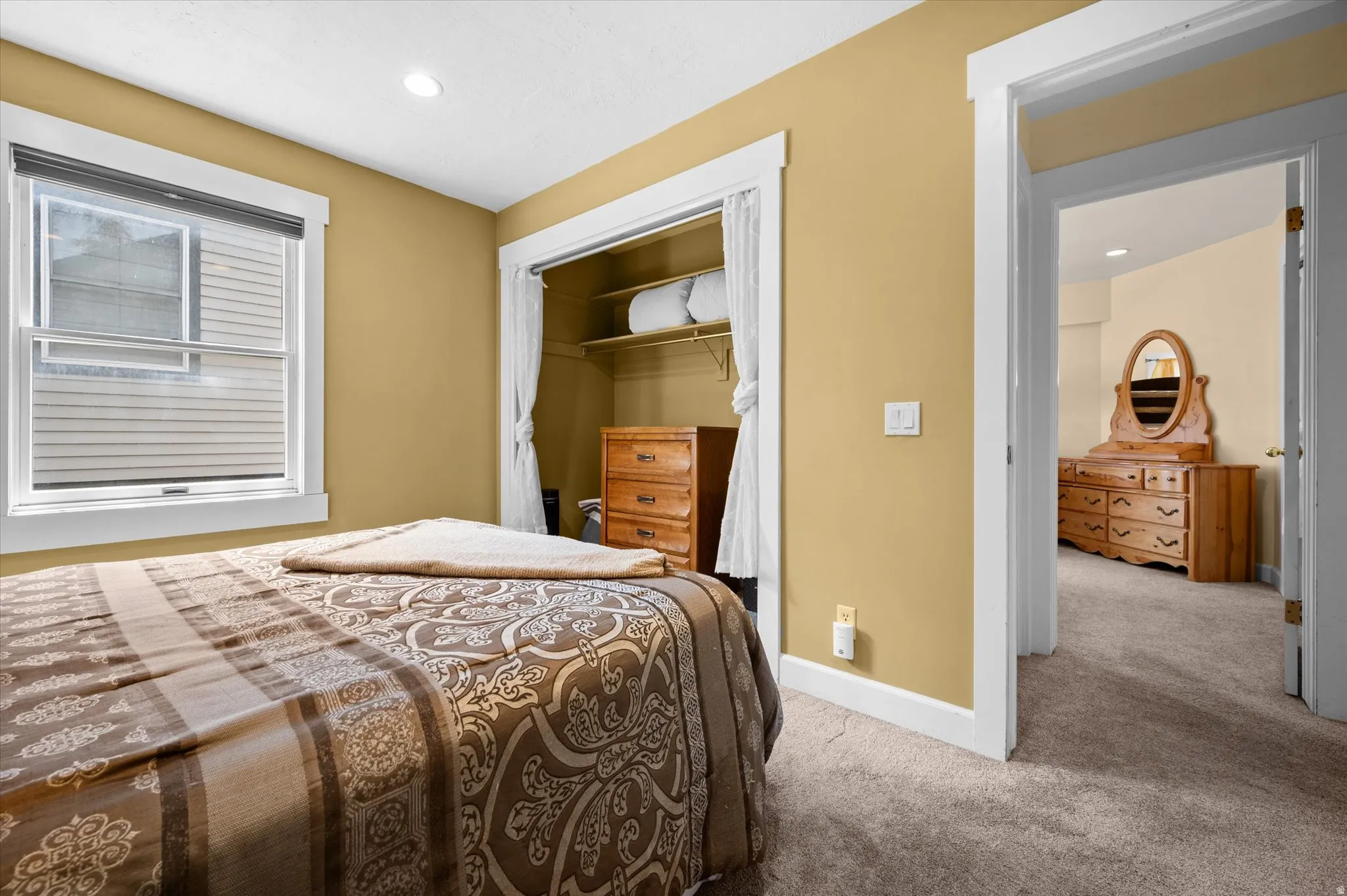 Additional guest bedroom with queen bed, storm window, and open closet with dresser.