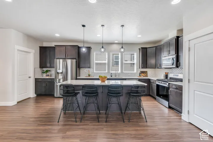 Kitchen featuring dark wood-finish cabinetry, stainless steel appliances, a center island with countertop seating, and wood-finish flooring