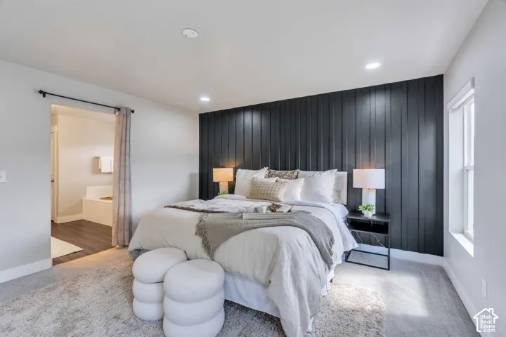 Accent wall with vertical paneling, recessed lighting, window with natural light, and a built-in tub in the background