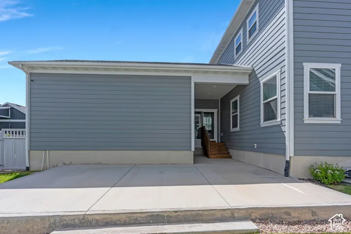 Spacious concrete patio with a covered entry, exterior siding, and multiple windows with white trim