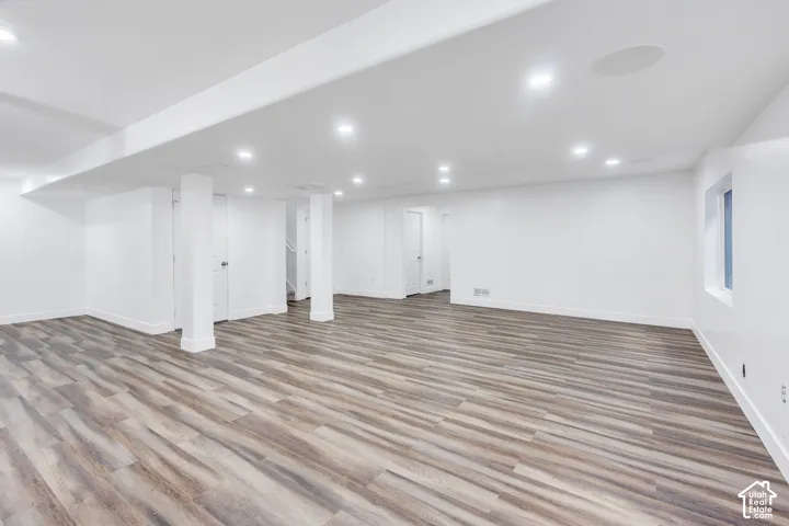 Spacious room with wood-finish flooring, recessed lighting, white walls, and a window