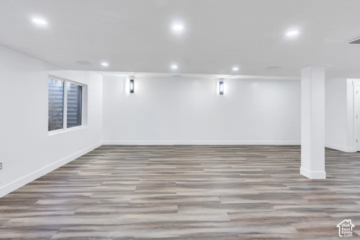 Wood-finish flooring, recessed lighting, and wall-mounted sconces illuminate this expansive room