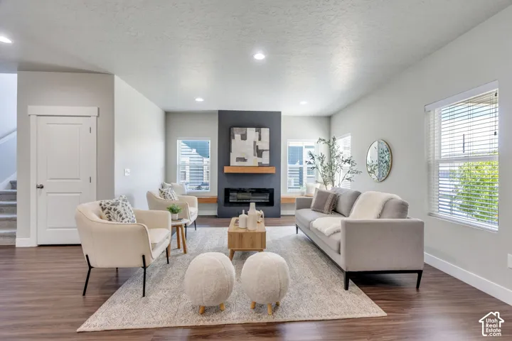 Sophisticated living room showcasing hardwood flooring, a linear fireplace with dark surround and wood mantel, recessed ceiling lighting, and expansive windows with plantation shutters