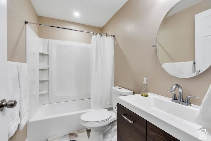 Full bathroom featuring a white tub/shower combination with built-in shelving, a toilet, a vanity with an integrated sink, and a circular wall-mounted mirror